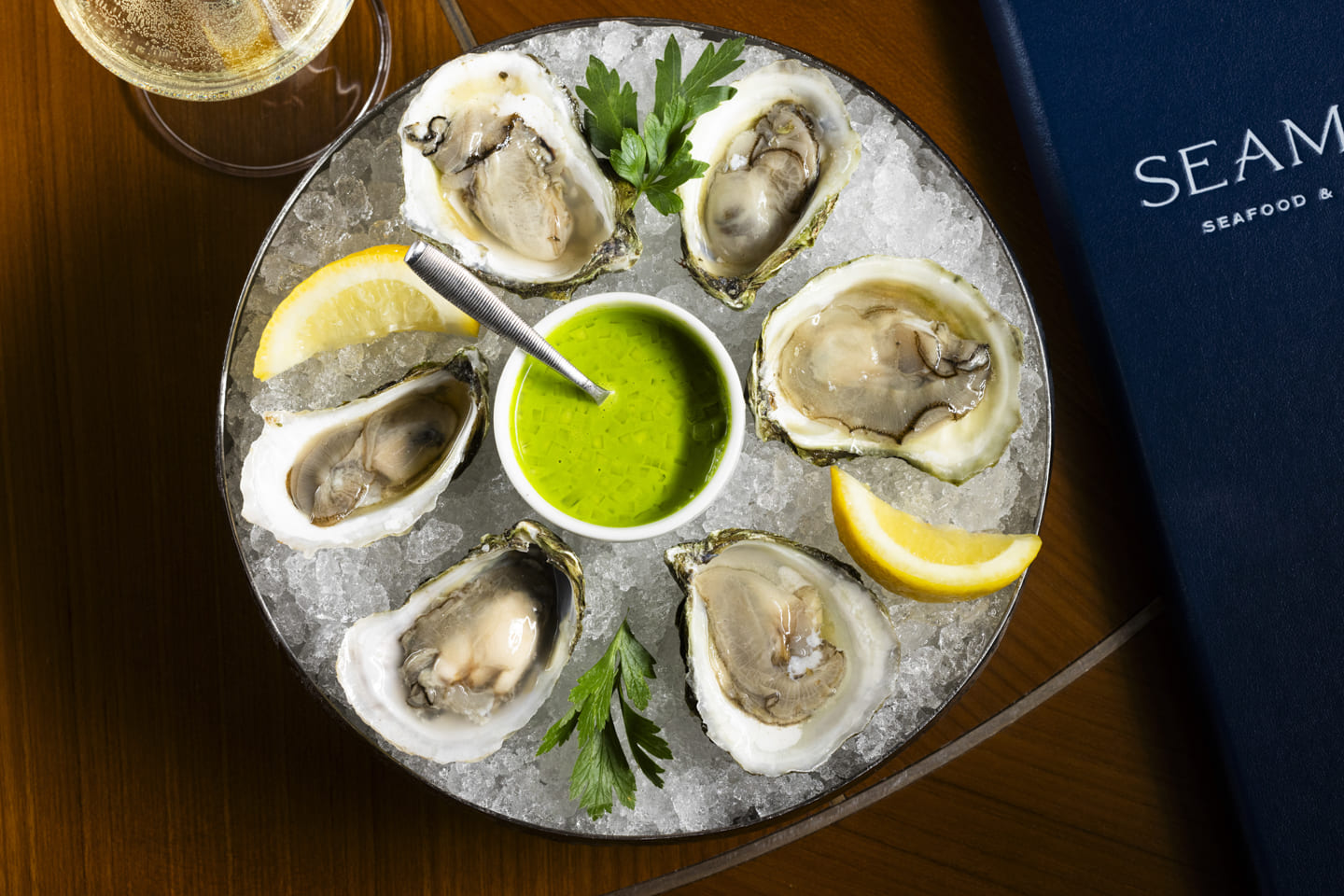 Restaurants at Encore Boston Harbor Resort A plate of fresh oysters served on ice with lemon wedges, parsley, and a vibrant green dipping sauce