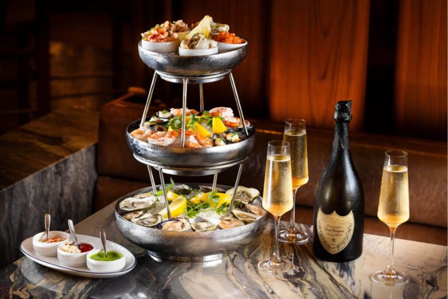 Restaurants at Encore Boston Harbor Resort Tiered seafood tower with oysters, shrimp, and champagne on a marble table